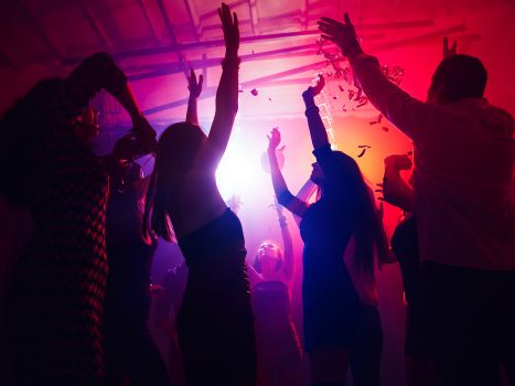 Eine Menschenmenge in Silhouette hebt ihre Hände gegen buntes Neonlicht auf Partyhintergrund